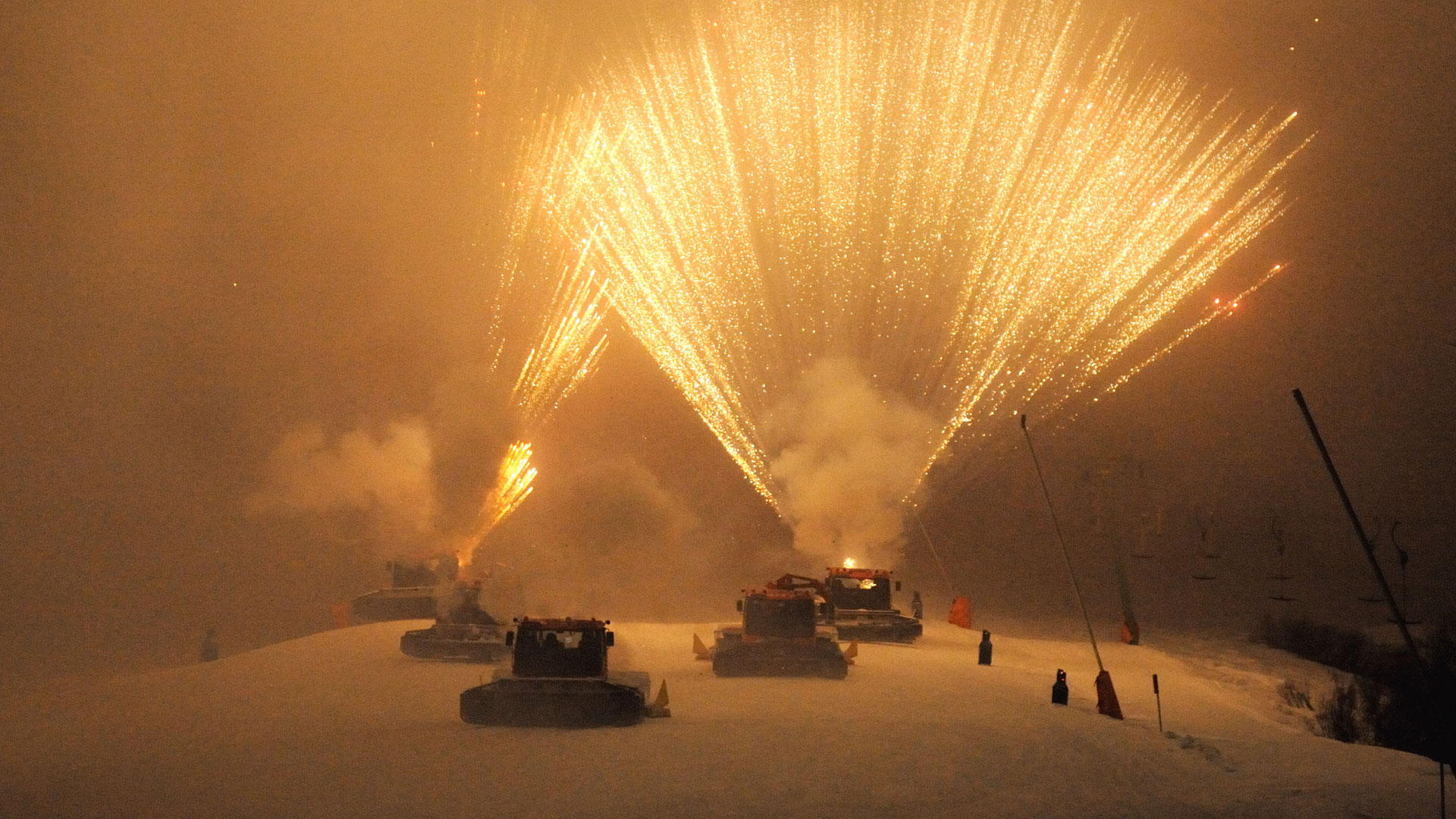 Pistenraupen feuern in der Nacht spektakuläre Feuerwerksfontänen in den Himmel.